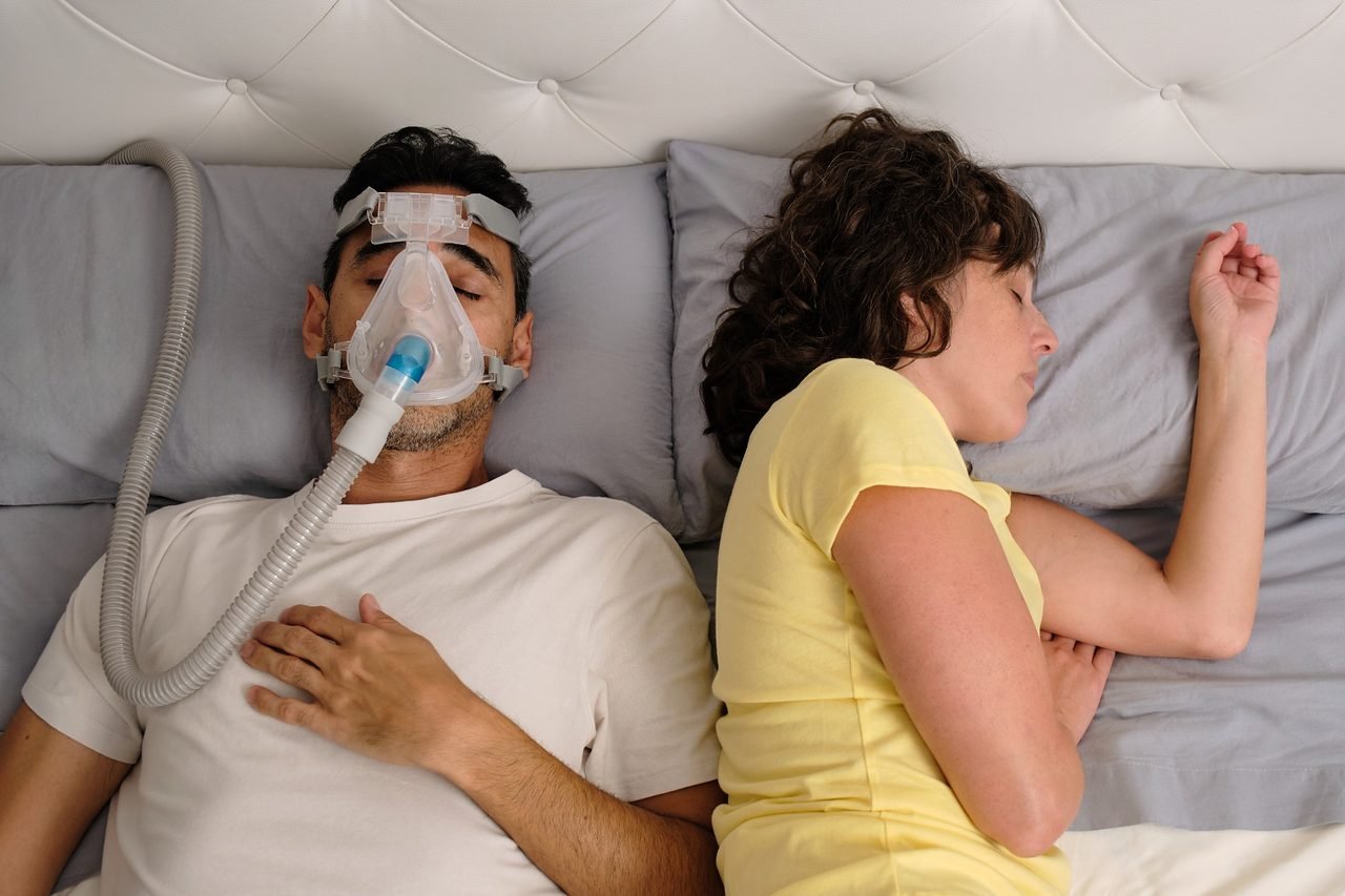 Breathing support at night after an airway evaluation Man sleeping on his back wearing a CPAP mask beside his partner