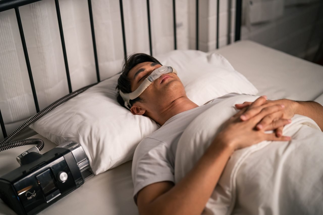 CPAP therapy and night-time breathing Man asleep in bed wearing a CPAP nasal mask with the machine beside him