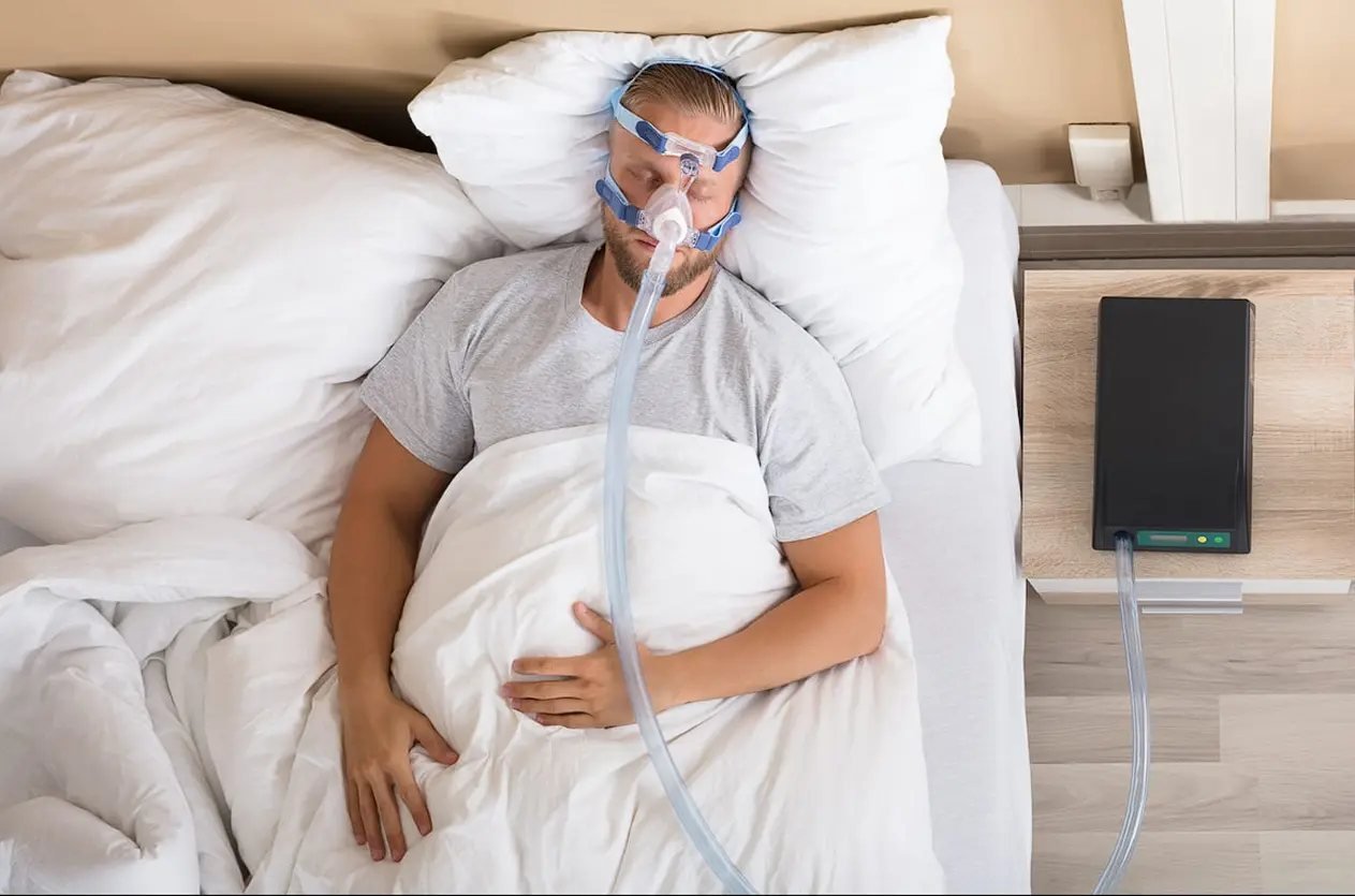 Traditional CPAP treatment for sleep apnea Man sleeping in bed wearing a bulky CPAP mask and straps, illustrating traditional sleep apnea treatment