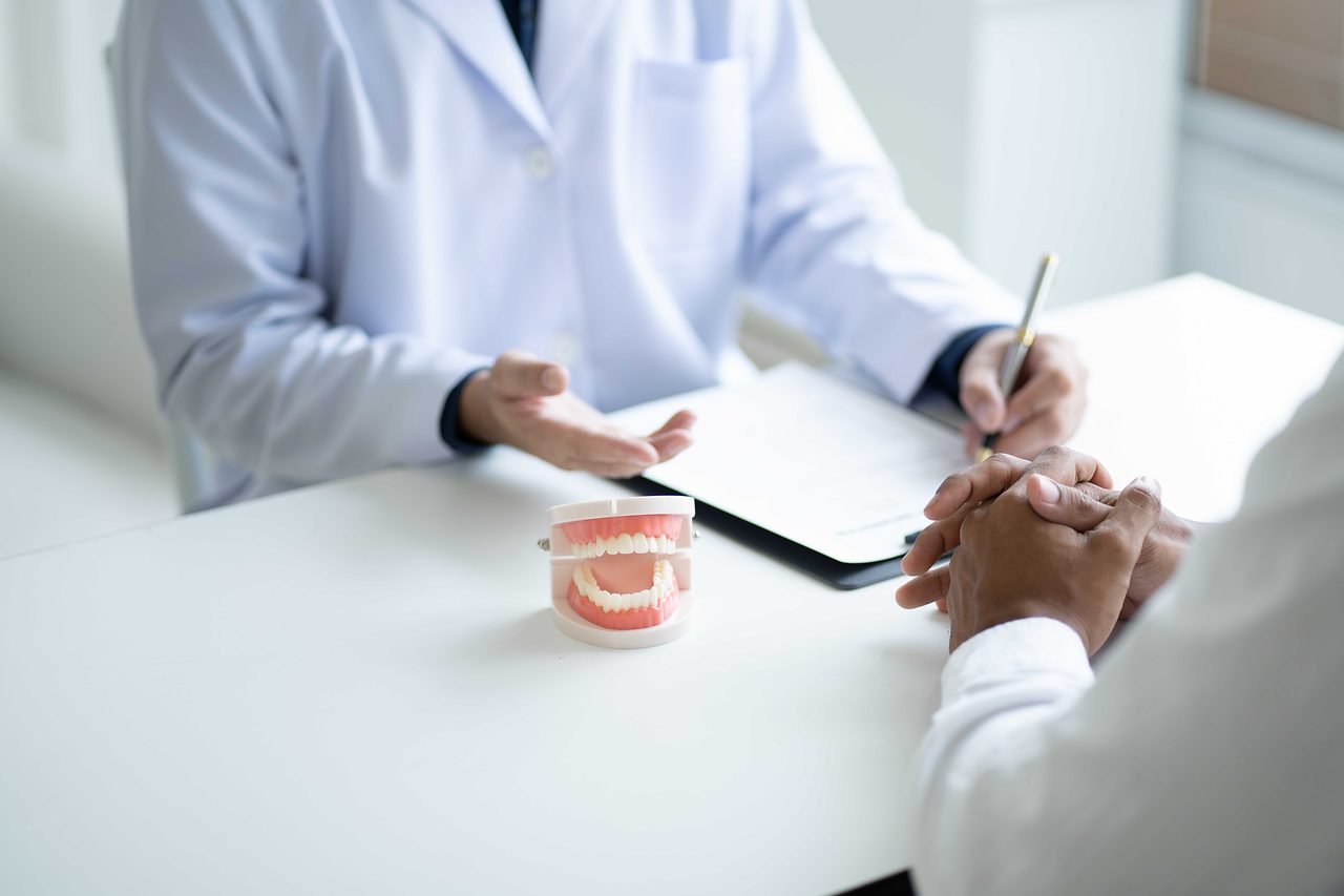 Dentist discussing treatment across a desk with a model of the teeth and jaw between them