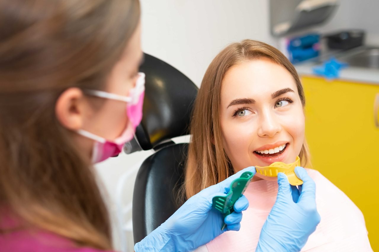 Dental assistant holding impression trays beside a smiling patient in the chair