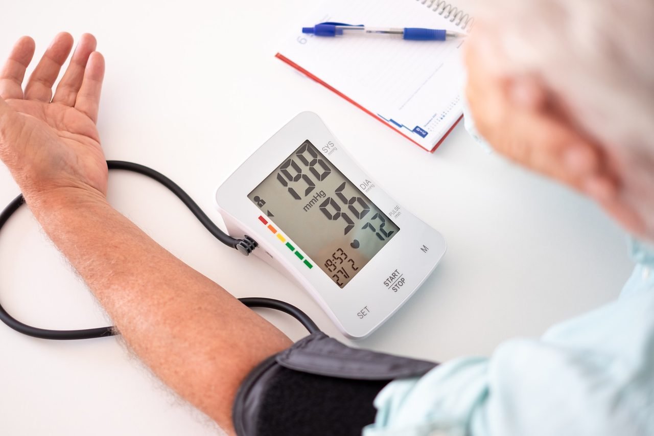 Older adult checking his blood pressure at home with an upper arm cuff and digital monitor