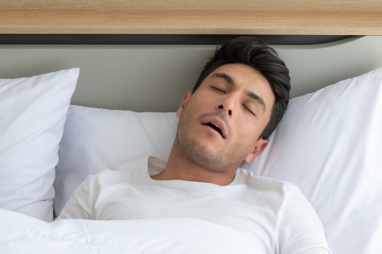 Man asleep on his back in bed with his mouth open