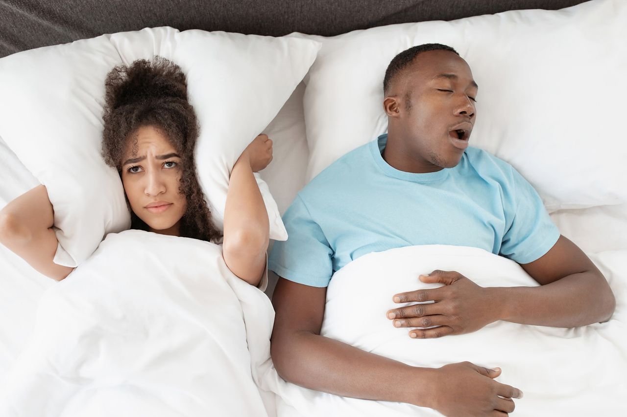 Snoring is common, but it is not always harmless Woman covering her ears with a pillow while her partner snores in bed