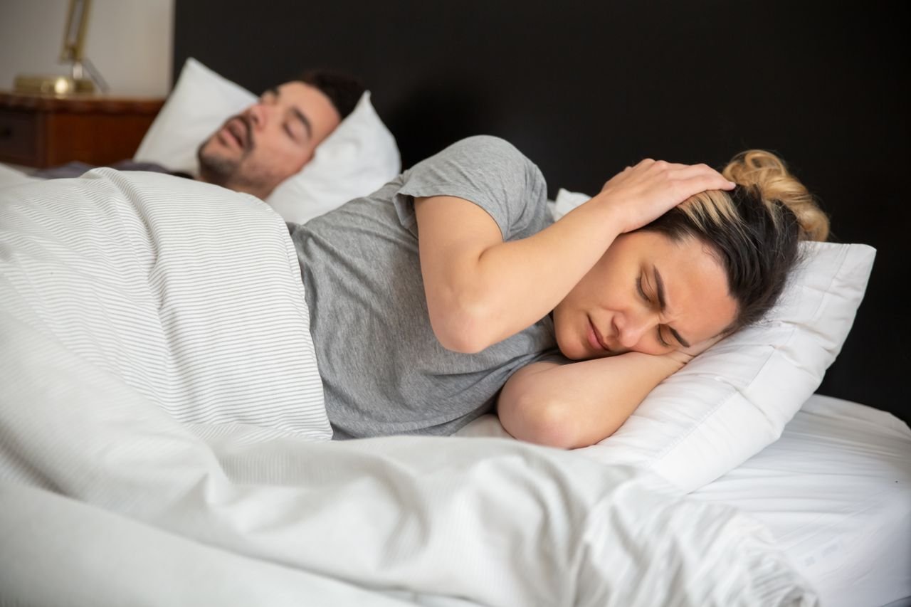 Snoring and sleep apnea affect both partners A man snoring in bed while his partner covers her ears