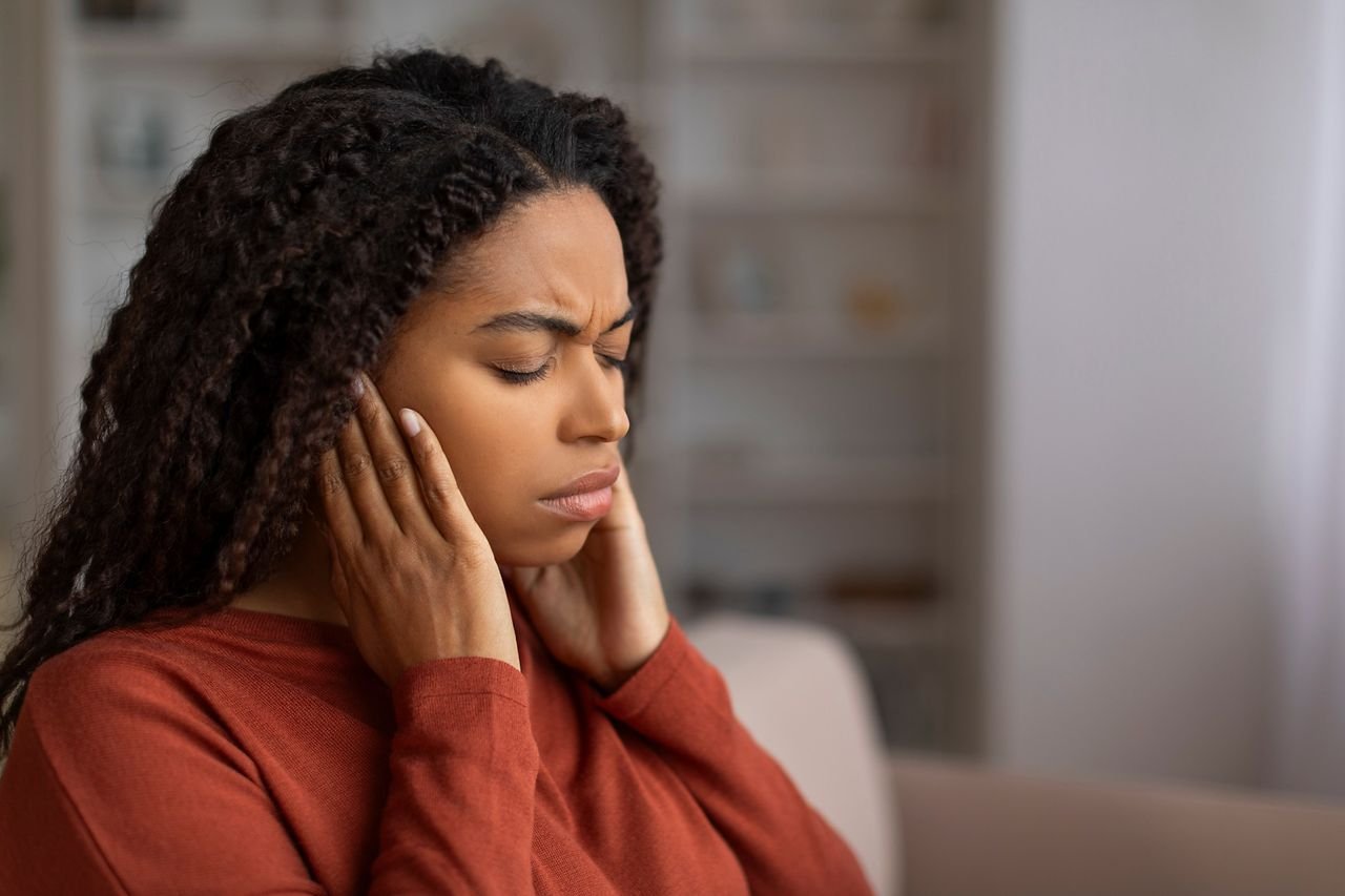 Jaw pain and headaches often show up together Woman pressing her hands to her jaw and ears in discomfort