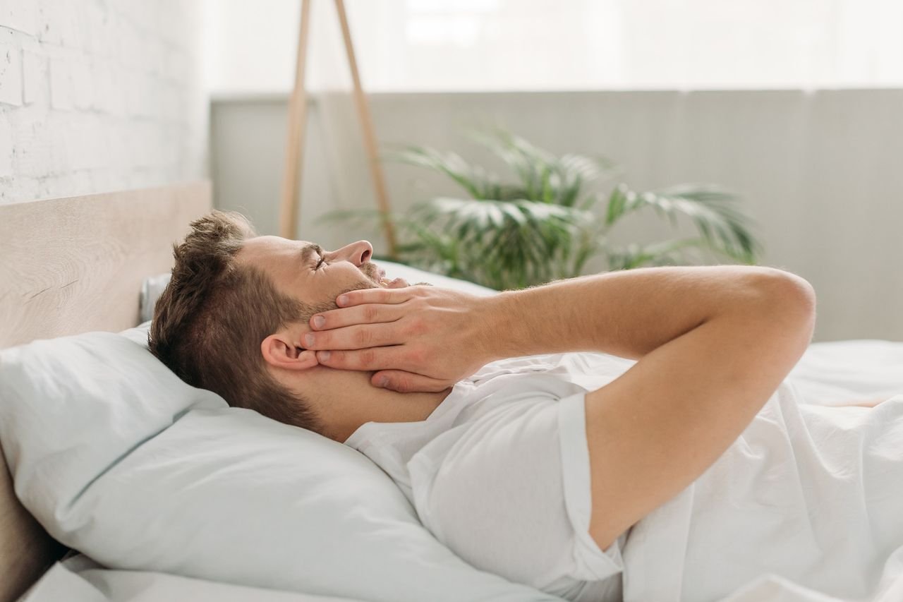 Headaches can be one of several TMD-related symptoms Man lying in bed holding his jaw in pain