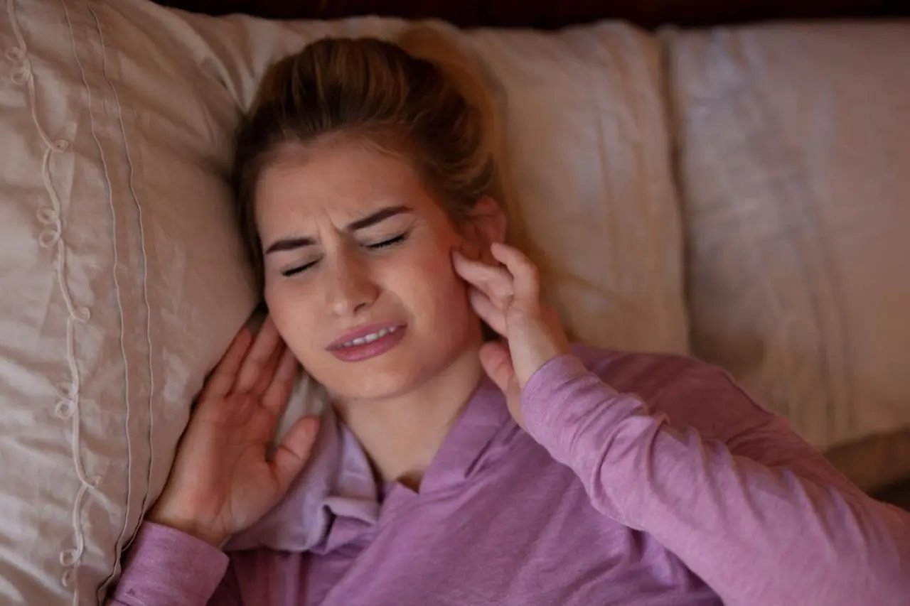 TMJ pain linked to airway and breathing issues Woman in bed touching her painful jaw, illustrating TMJ pain and teeth grinding linked to airway issues